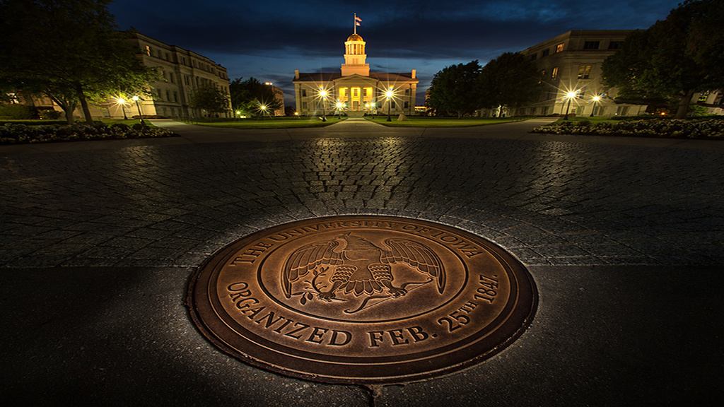 the university of iowa seal in front of the UI Capitol at night